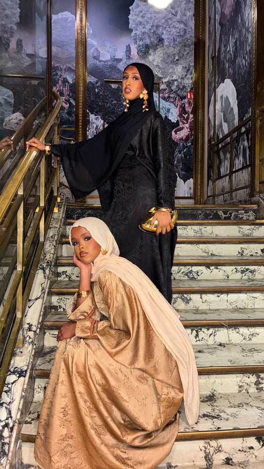 Onyx Jacquard Abaya – black satin abaya styled on a marble staircase